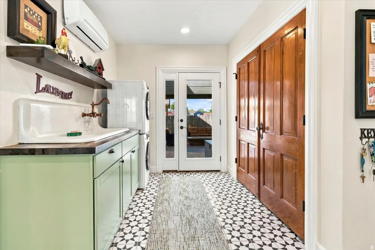 Laundry area featuring patterned floor tile, light green cabinetry with a solid surface countertop, white basin sink with a wall-mounted faucet, and double French doors with external access