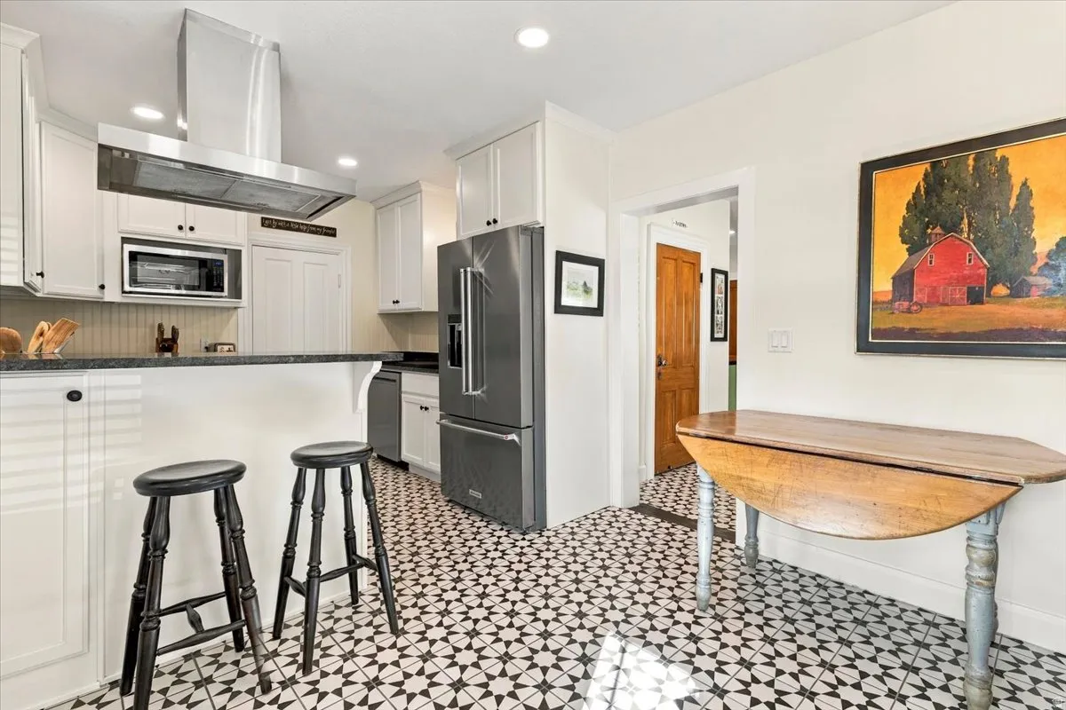 Kitchen featuring white cabinetry, stainless steel appliances, dark countertops, and patterned floor tile