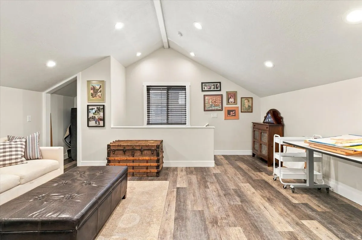 Vaulted ceiling with recessed lighting, wood-finish flooring, and a window with blinds