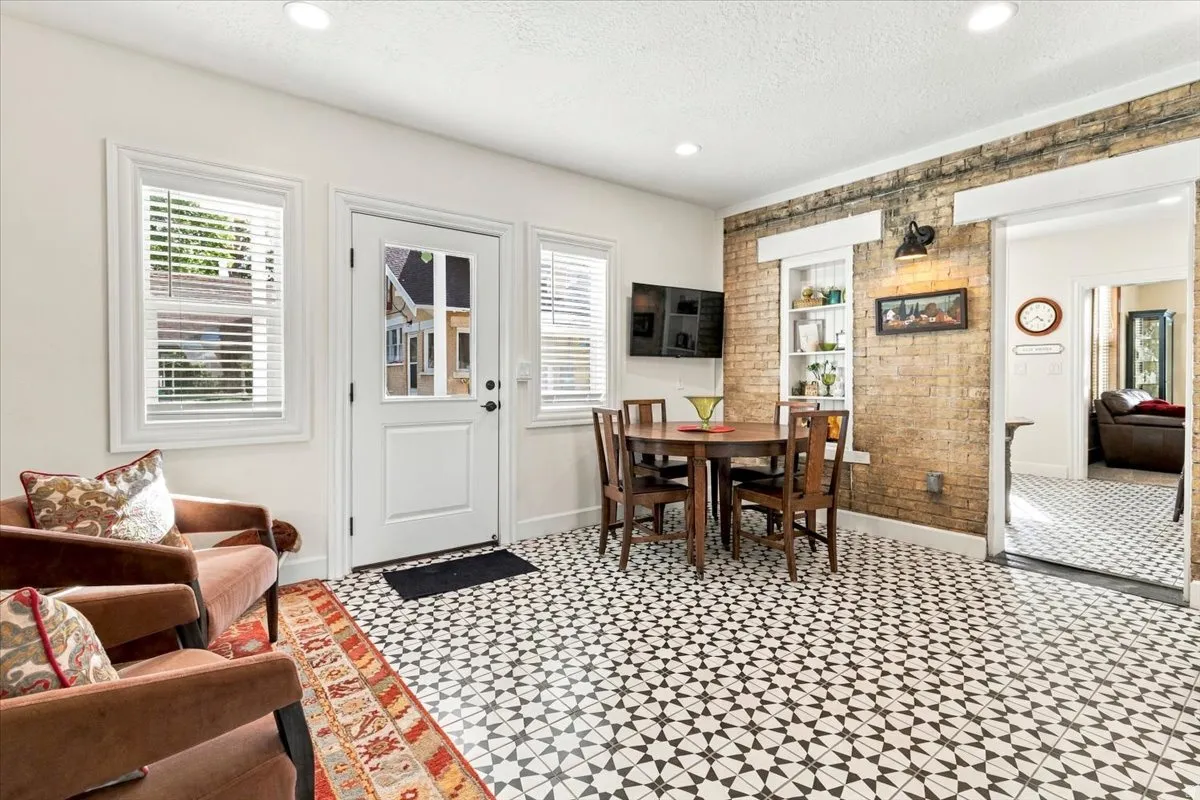 Patterned tile flooring, exposed brick wall, built-in shelving, white trim windows, and a glass-paneled door