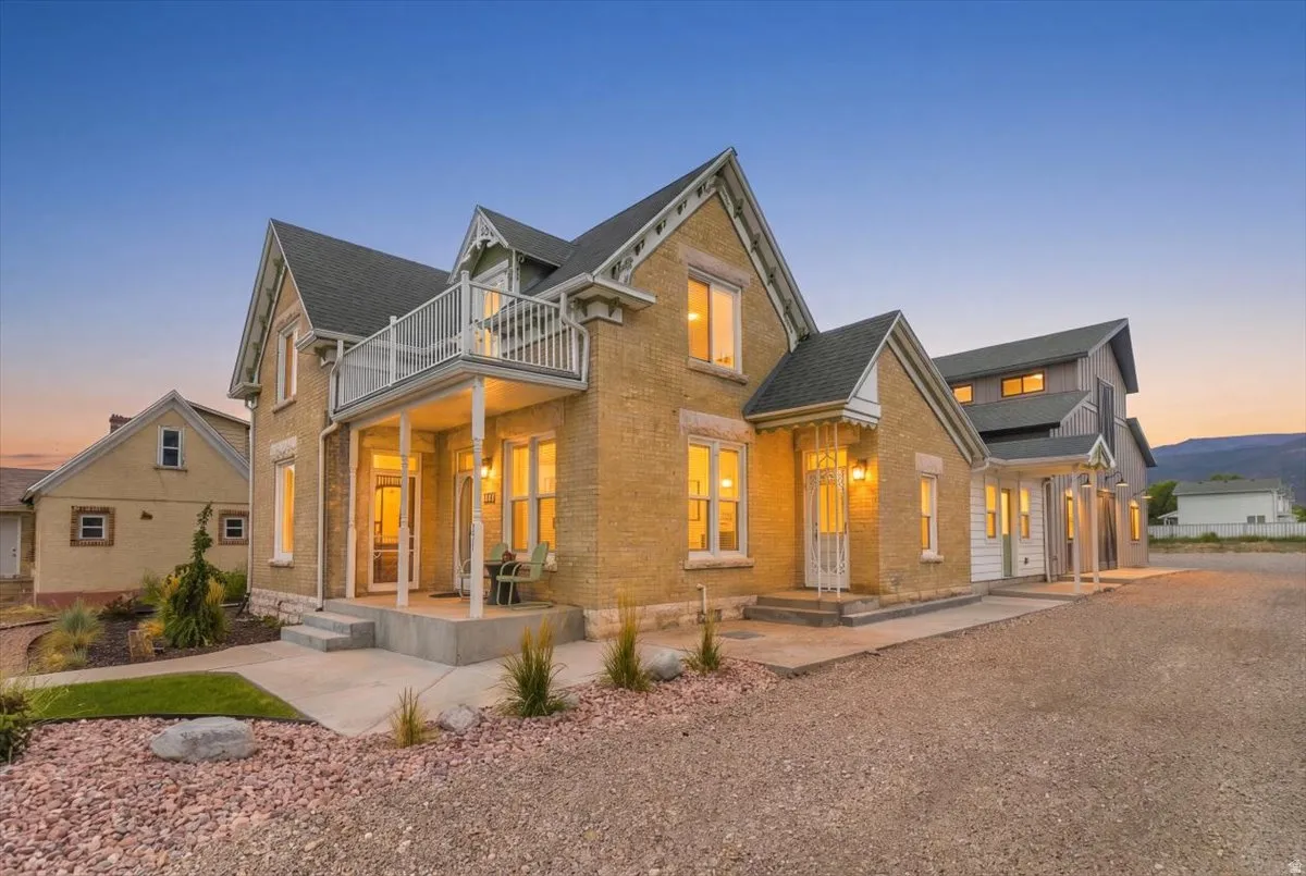 Elegant brick farmhouse with multiple gabled rooflines and stone accents, featuring illuminated windows and an attached covered porch