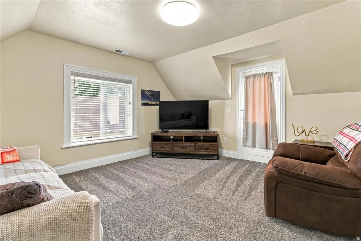 Vaulted ceilings, neutral wall tones, window with horizontal blinds, carpeted flooring, and a built-in media console