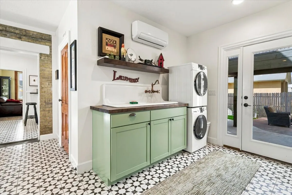 Patterned floor tiles, wall-mounted air conditioning unit, built-in cabinetry with sink, stacked laundry appliances, and double glass doors