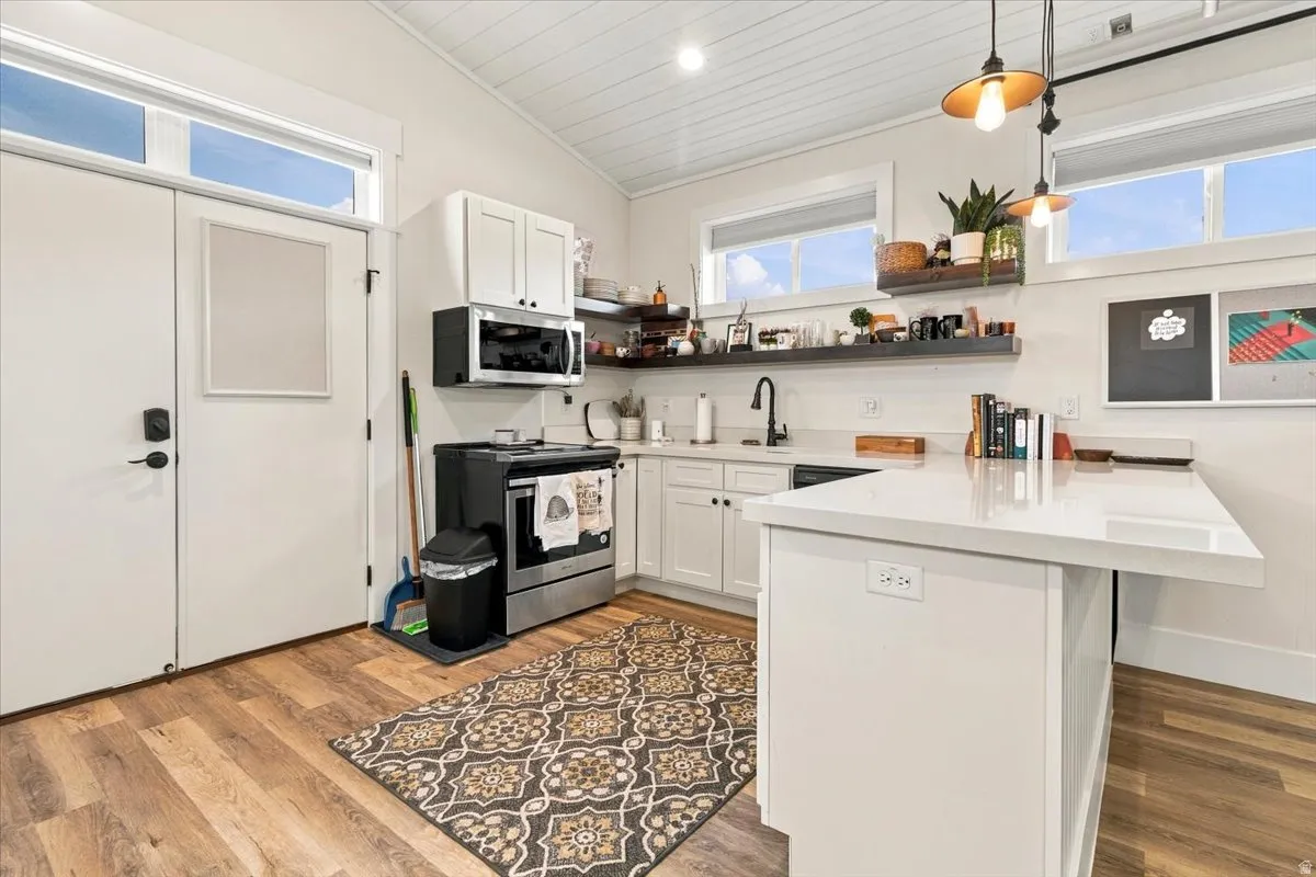 Wood-finish flooring, white cabinetry, stainless steel appliances, white countertops, and beadboard ceiling