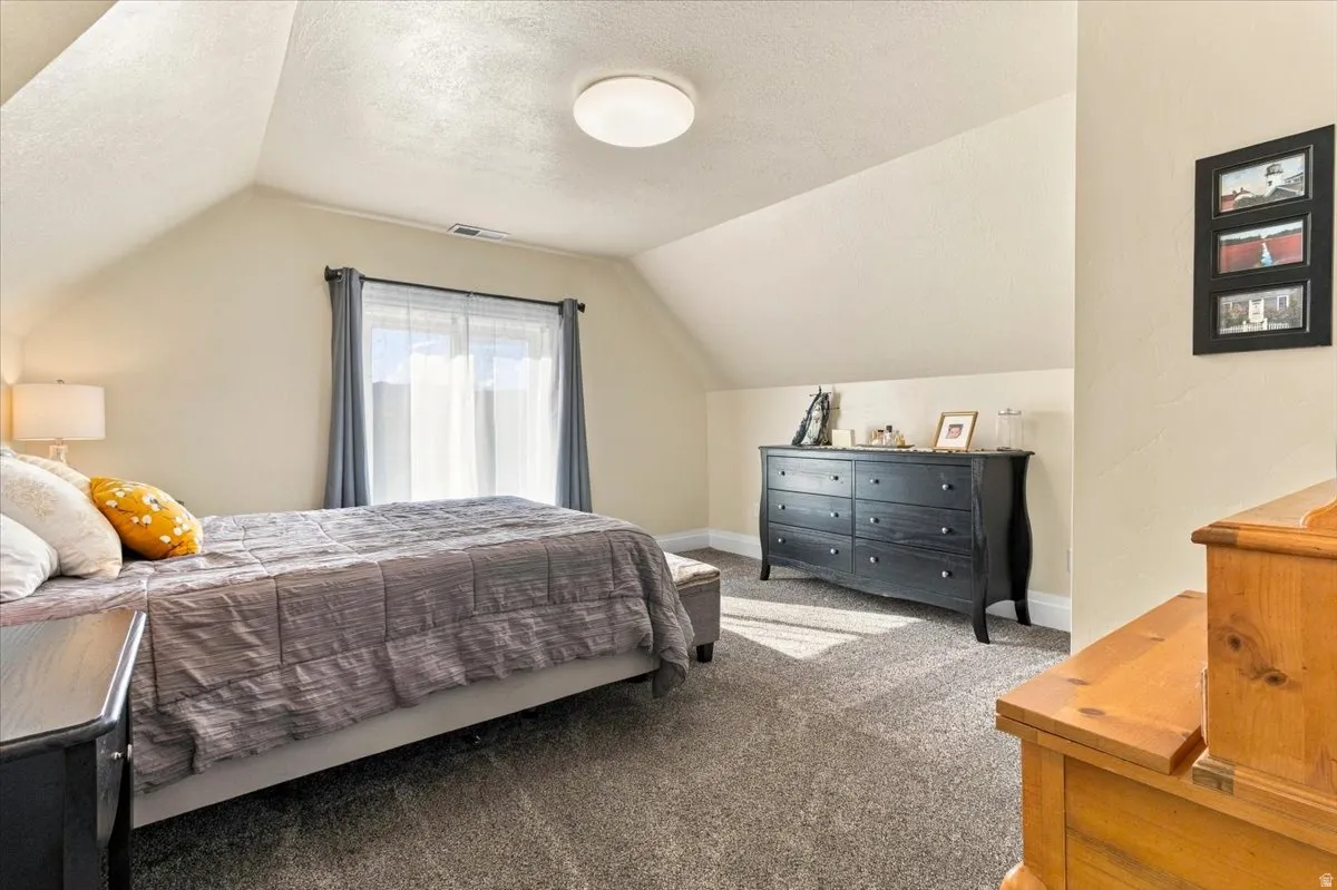 Bright second-floor bedroom featuring vaulted ceilings, recessed lighting, and a large window with natural light