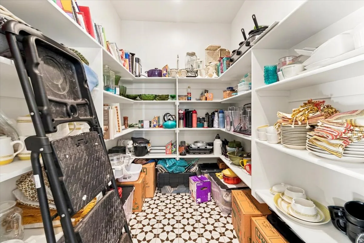 Extensive storage pantry with multiple built-in white shelves and a patterned floor tile
