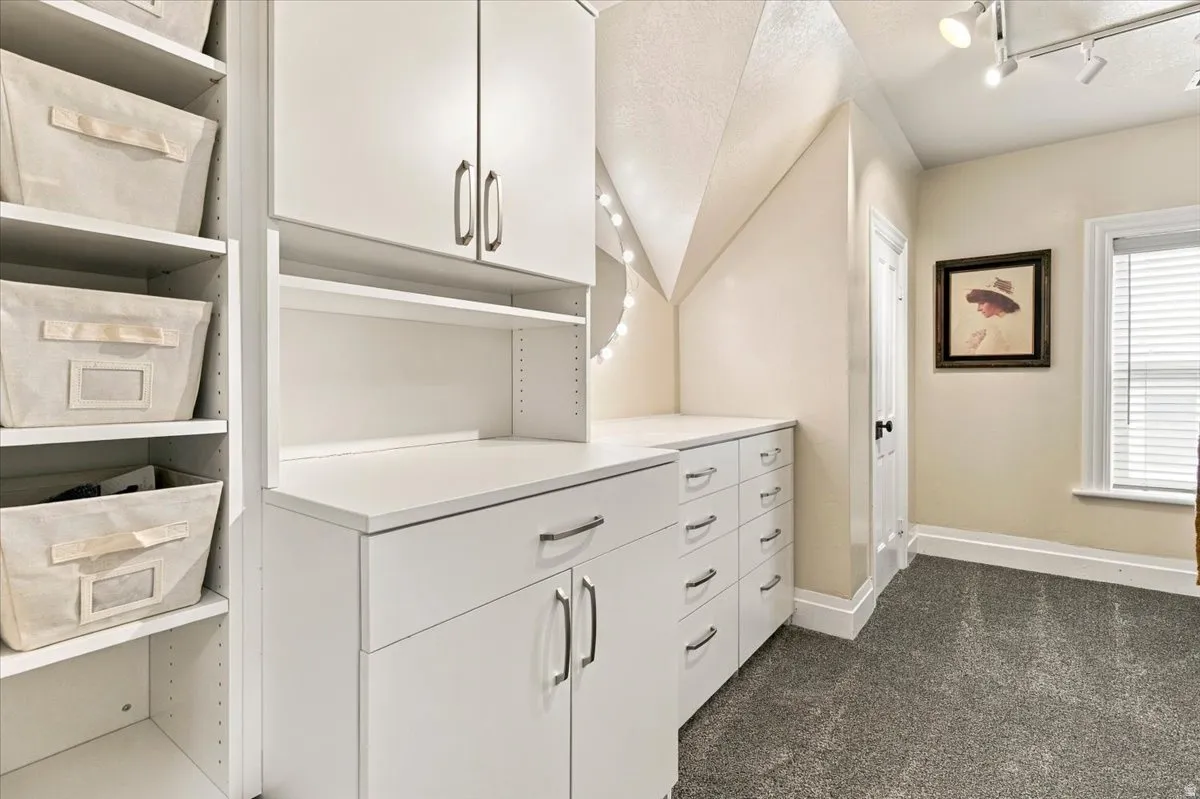 White cabinetry with metal hardware, built-in shelving, track lighting, and a window with blinds