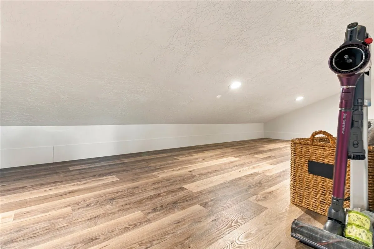 Angled ceiling with recessed lighting, wood-finish flooring, and white wall paneling