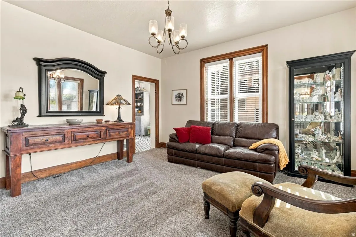 Recessed lighting and a chandelier illuminate the carpeted living area, featuring a window with wood trim and blinds