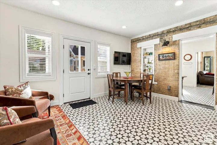Patterned tile flooring, exposed brick wall, built-in shelving, white trim windows, and a glass-paneled door