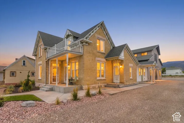Elegant brick farmhouse with multiple gabled rooflines and stone accents, featuring illuminated windows and an attached covered porch