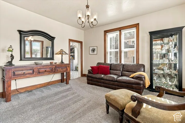 Recessed lighting and a chandelier illuminate the carpeted living area, featuring a window with wood trim and blinds