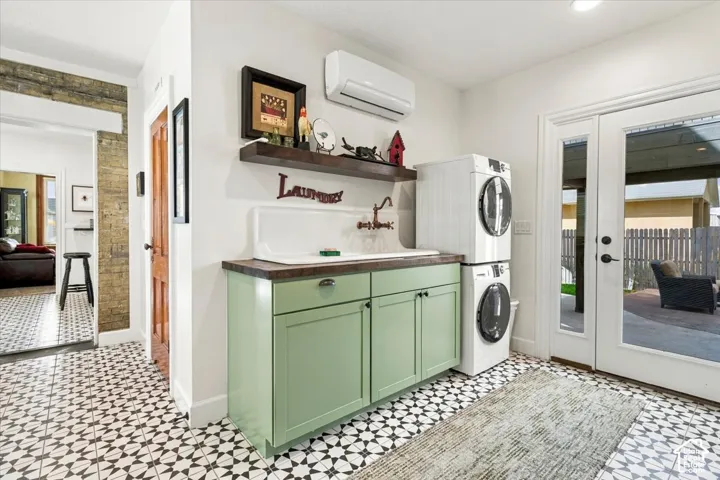Patterned floor tiles, wall-mounted air conditioning unit, built-in cabinetry with sink, stacked laundry appliances, and double glass doors