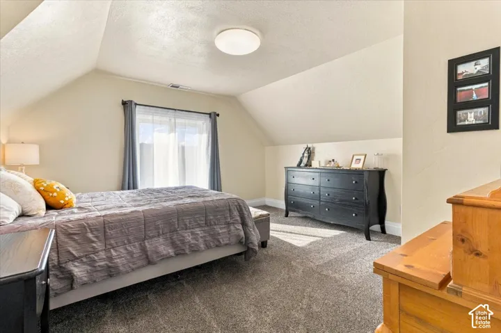 Bright second-floor bedroom featuring vaulted ceilings, recessed lighting, and a large window with natural light