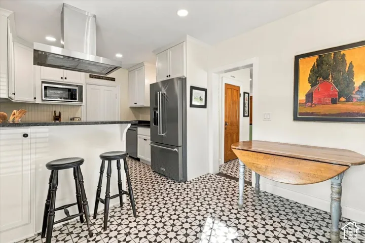 Kitchen featuring white cabinetry, stainless steel appliances, dark countertops, and patterned floor tile