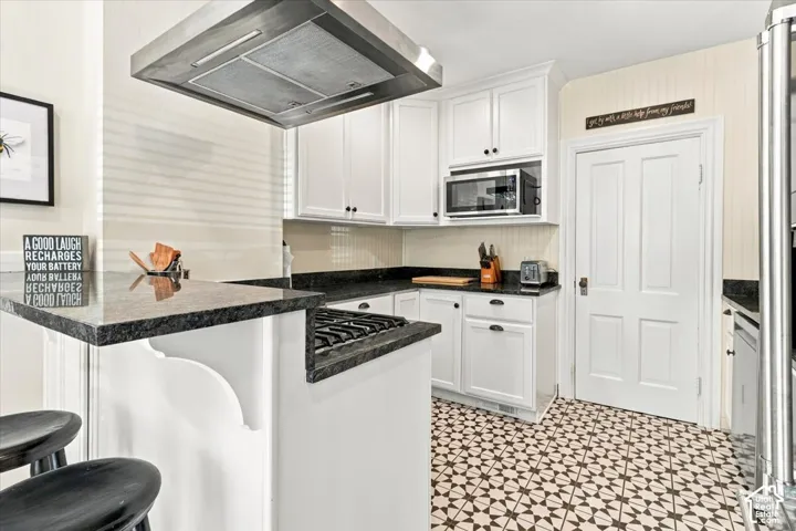 White cabinetry with dark hardware, built-in microwave, stainless steel range hood, patterned floor tile, and a four-panel interior door