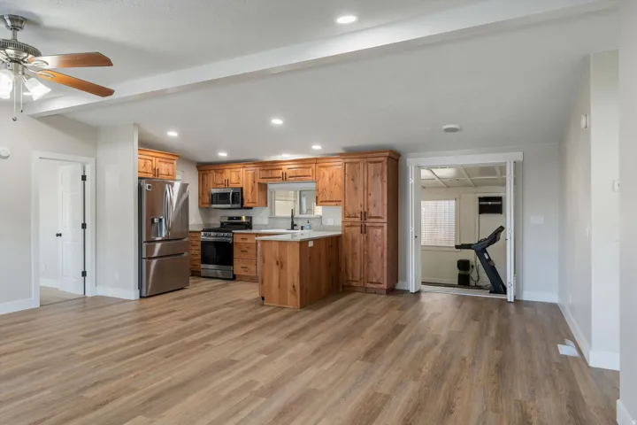 Wood-finish flooring throughout, kitchen with stainless steel appliances, wood cabinetry, stone-look countertops, and an island