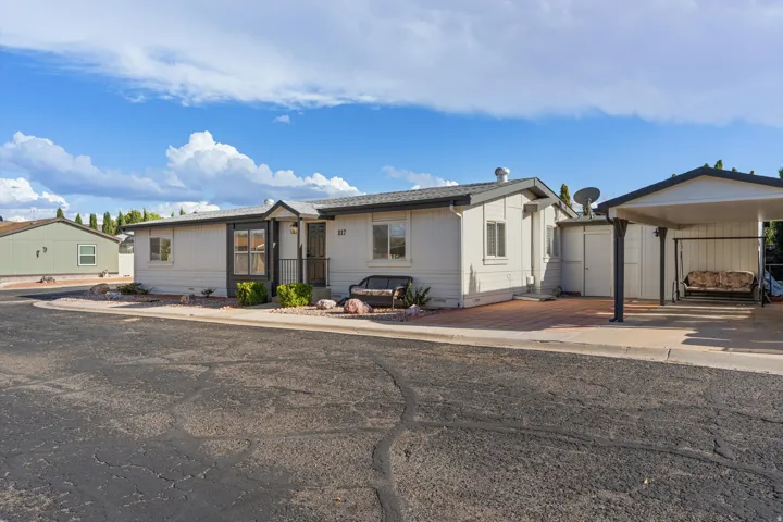 White exterior with dark trim accents, covered entry, attached carport, and a paver patio area