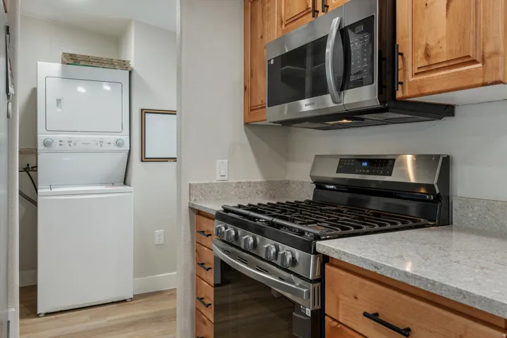 Stainless steel gas range, stainless steel microwave, light-toned wood cabinetry, stone-finish countertops, and wood-finish flooring