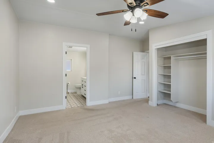 Integrated ceiling fan with light fixture, recessed lighting, wall-to-wall carpeting, open closet with shelving and hanging rod, and an en-suite bathroom with a window