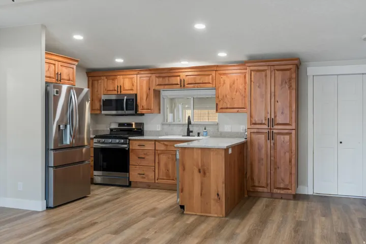 Kitchen featuring wood-finish cabinetry, stainless steel appliances, a center island with a light-toned countertop, and recessed lighting