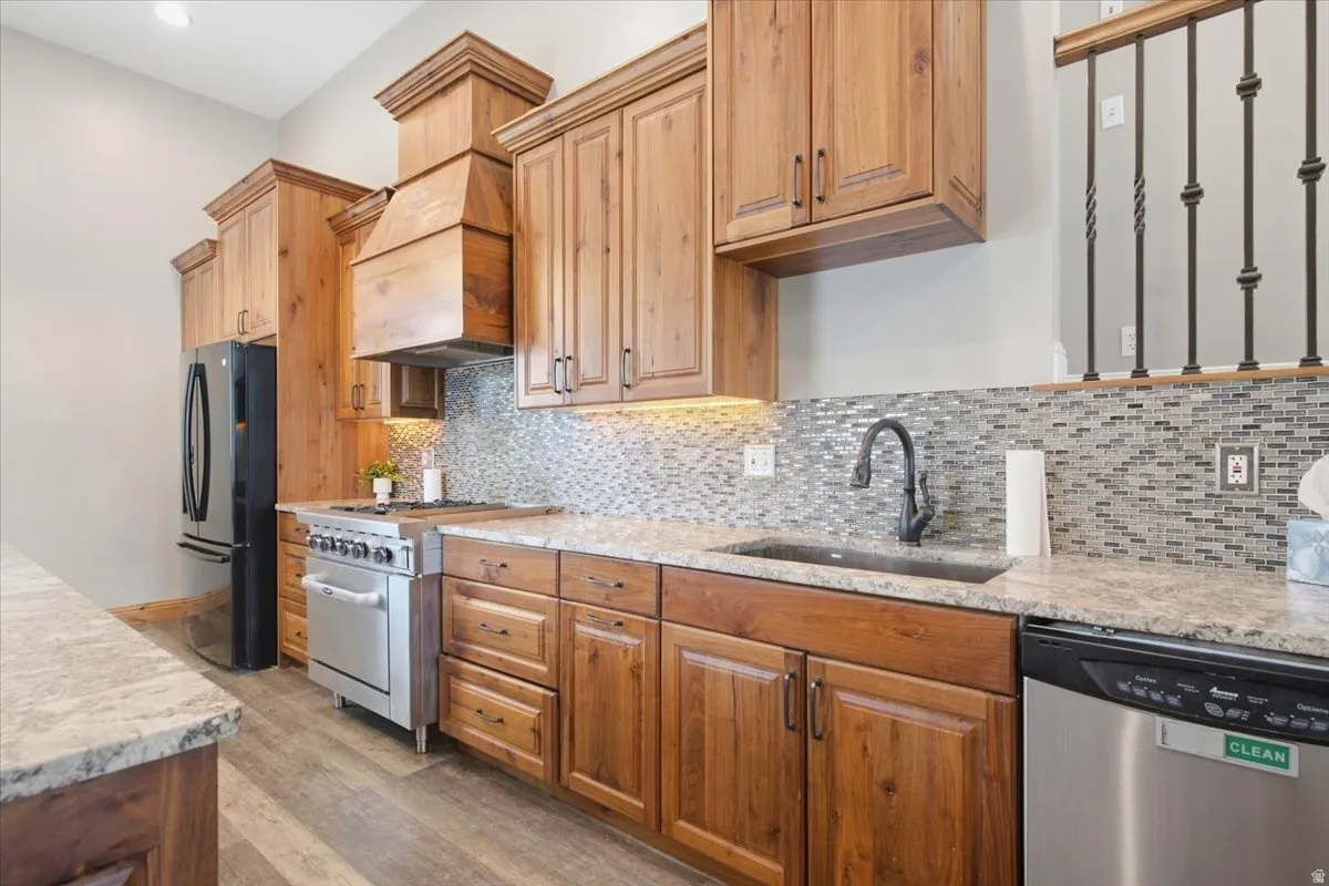 Wood-finish cabinetry with decorative crown molding, stainless steel appliances, stone countertops, mosaic tile backsplash, and wood-finish flooring