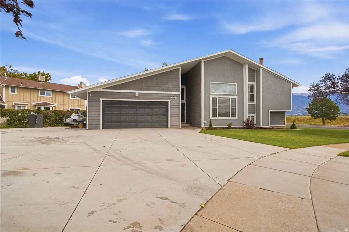 Contemporary gray exterior featuring varied siding materials, a prominent two-car garage, and an expansive concrete driveway