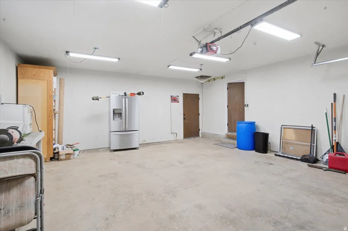 Spacious garage with concrete flooring, multiple overhead light fixtures, and two interior doors