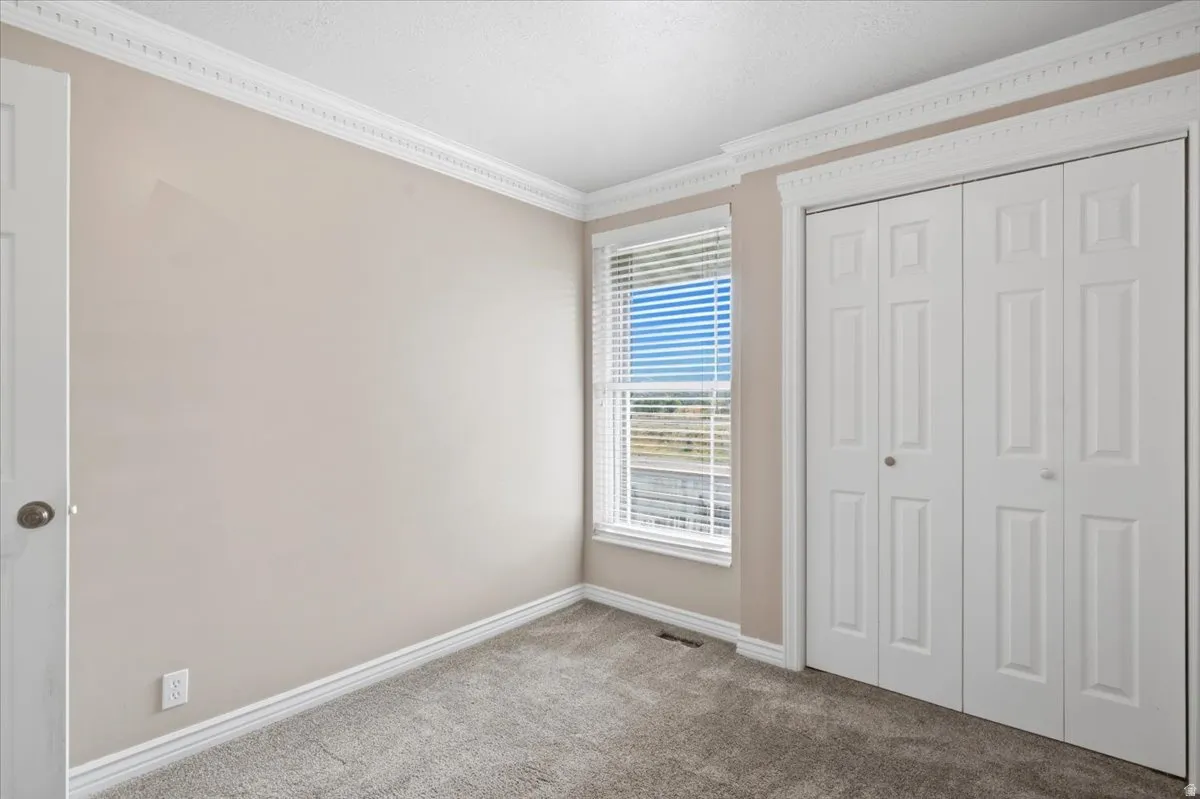 Carpeted room featuring a window with blinds, bi-fold doors, crown molding, and baseboards