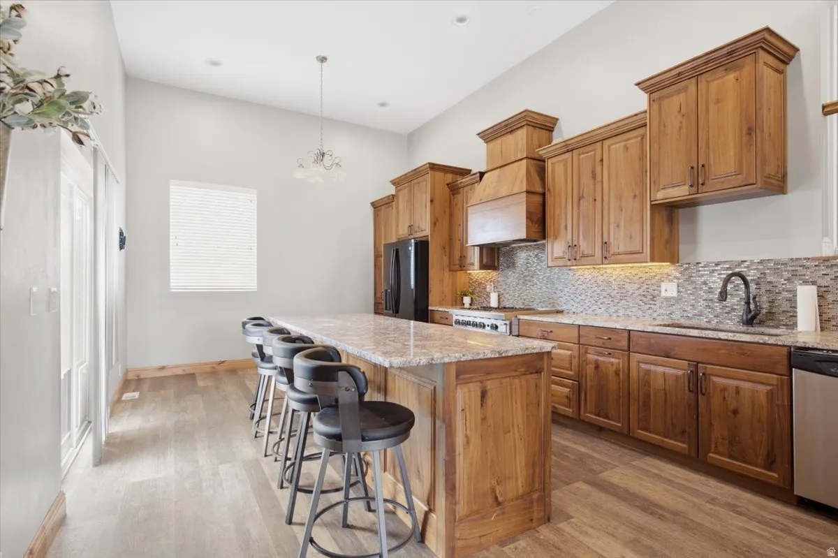 Vaulted ceiling, wood-finish flooring, natural wood cabinetry, mosaic tile backsplash, and a spacious kitchen island
