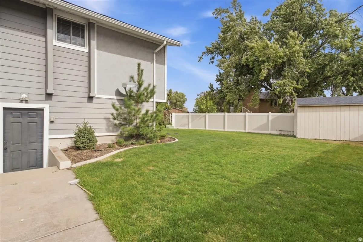 Expansive lawn area, concrete pathway, privacy fencing, exterior storage shed, and mature trees