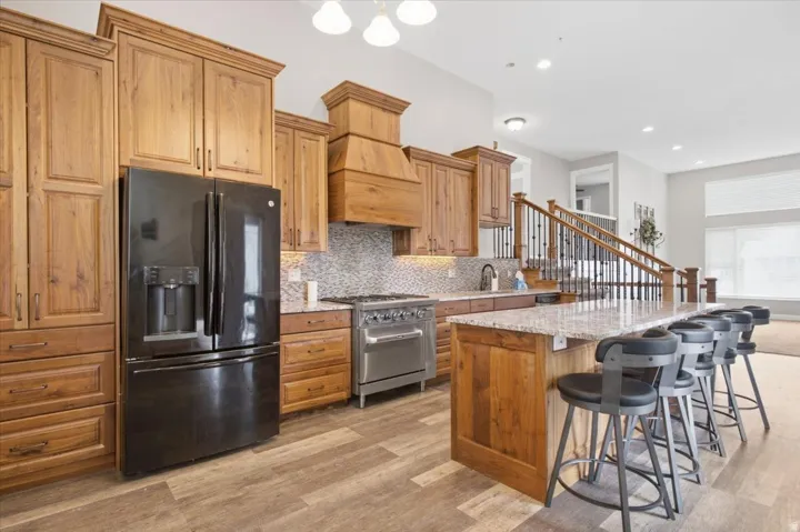 Kitchen featuring extensive wood cabinetry, wood-finish flooring, a stainless steel range, and a spacious island with a stone countertop