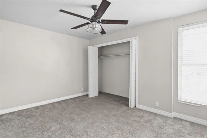 Soft gray carpeting, neutral wall palette, ceiling fan with integrated lighting, window with blinds, and bi-fold closet doors