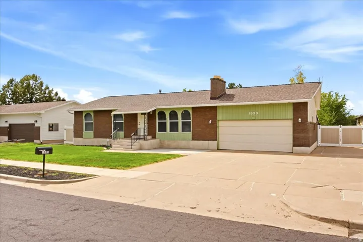 Brick and siding exterior with a concrete driveway, attached garage, front lawn, and privacy fencing