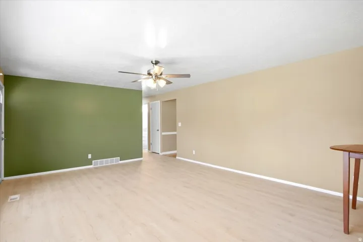 Spacious room featuring light wood-finish flooring, a ceiling fan with integrated lighting, and a neutral color palette