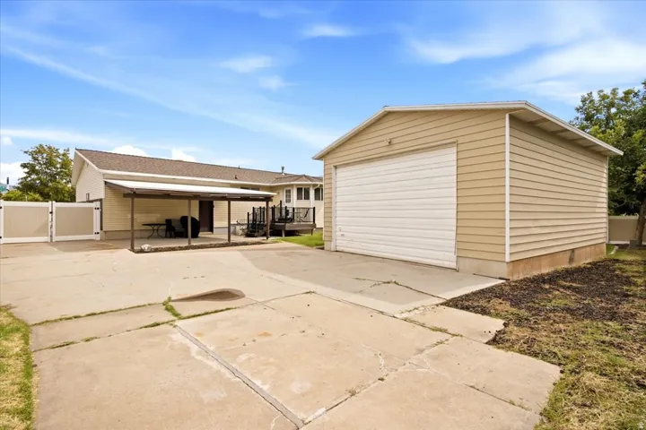Detached garage with horizontal siding, a private covered patio, a concrete patio, and a privacy fence