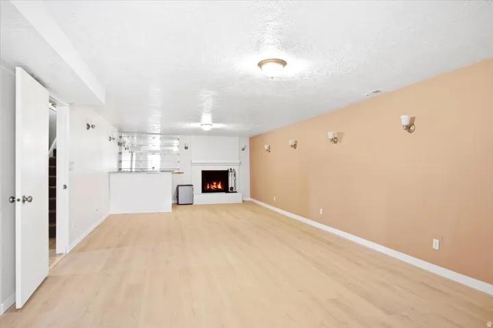 Spacious room featuring light wood-finish flooring, a white mantel fireplace, and a built-in bar area with mirrored shelving