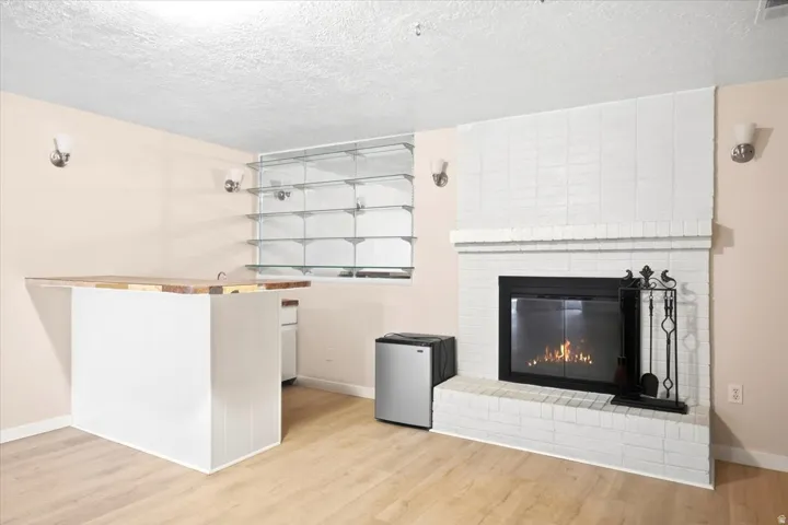 White brick fireplace, light wood-finish flooring, built-in bar with wood countertop, built-in glass shelving, and wall sconce lighting
