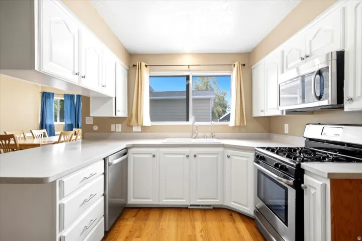 White cabinetry with brushed nickel hardware, stainless steel appliances, solid surface countertops, a built-in dishwasher, and wood-finish flooring
