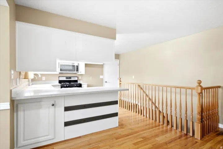 Kitchen area with white cabinetry, a built-in microwave, and a black range