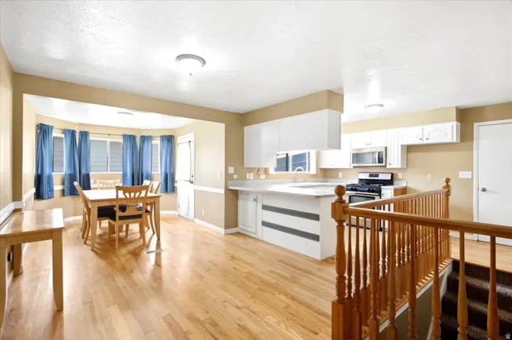 Hardwood-style flooring throughout, white upper and lower cabinetry, stainless steel appliances, and a bay window in the dining area