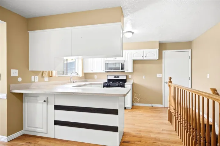 Kitchen featuring white cabinetry, light countertops, wood-finish flooring, and stainless steel appliances