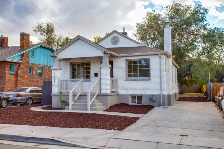 White brick exterior with a front porch, concrete steps, and a paved driveway