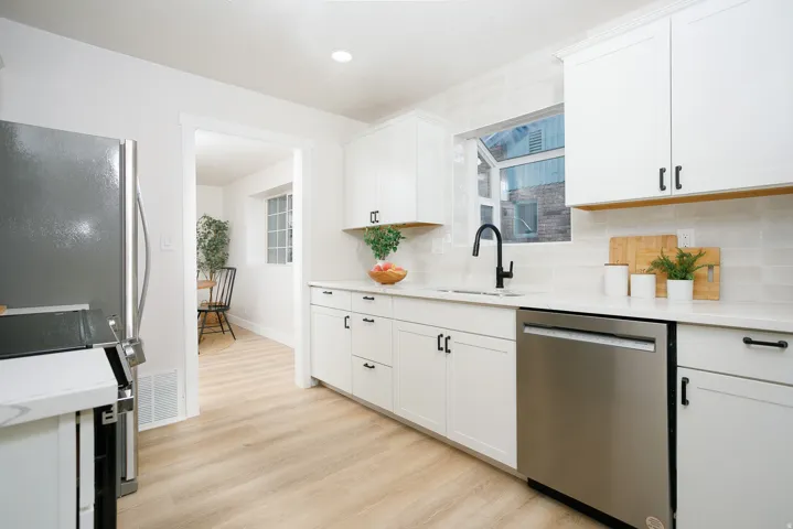 Modern kitchen featuring white shaker cabinetry, stainless steel appliances, light wood-finish flooring, and a subway tile backsplash