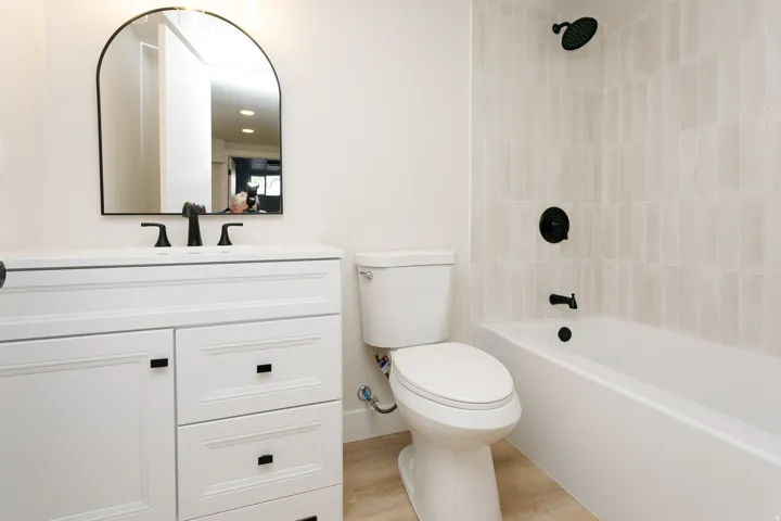 Modern bathroom featuring a white vanity with multi-drawer storage and matte black hardware, paired with a sleek arched mirror and matte black faucet