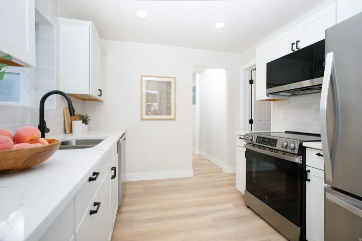 White cabinetry with matte black hardware, stainless steel appliances, light wood-finish flooring, white countertops, and recessed lighting
