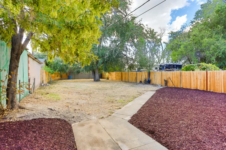 Spacious backyard with a new wooden fence, concrete pathway, decorative mulch beds, and mature trees