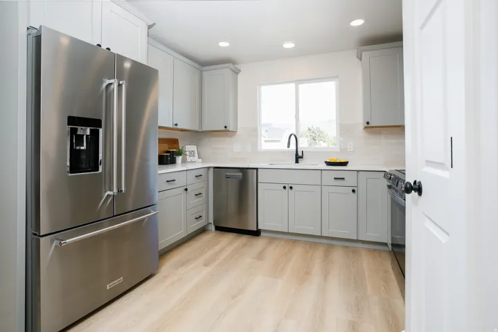 Kitchen featuring stainless steel appliances, light wood-finish flooring, light gray cabinetry with black hardware, and a window above the sink