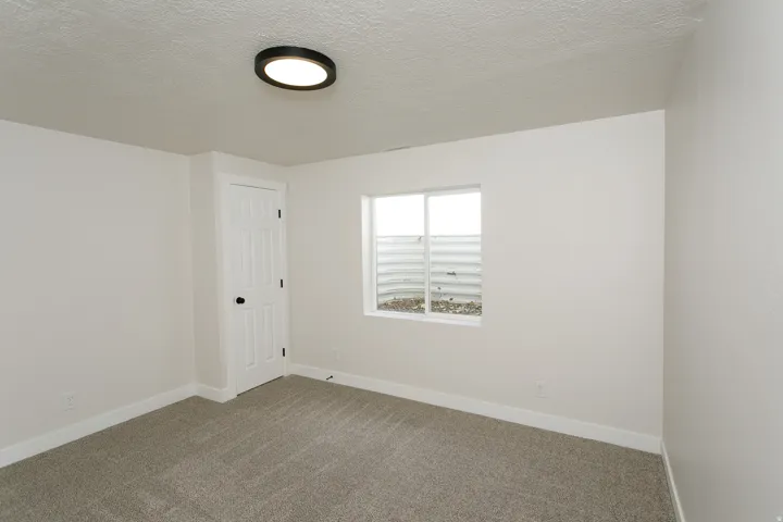 White walls with neutral carpeting, white trim, a modern flush-mount light fixture, and a window