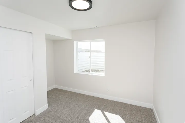 White walls, carpet flooring, flush mount ceiling light, white trim, and a window
